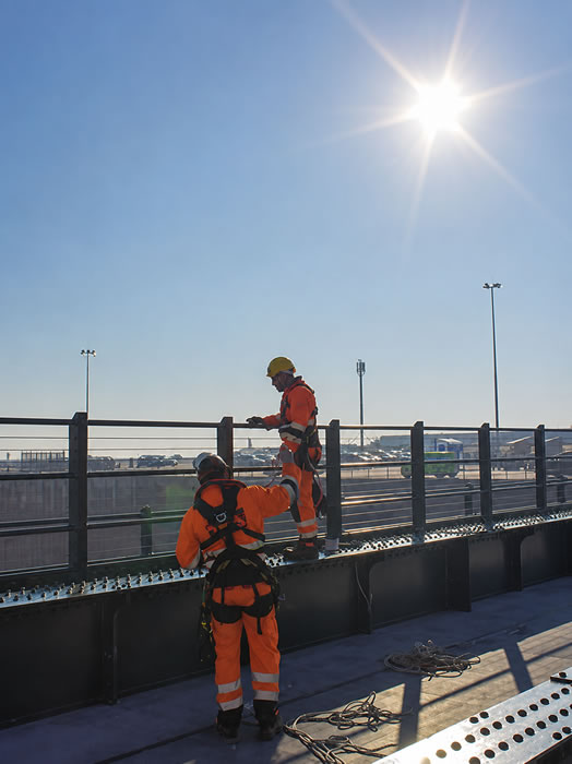 Two rope access technicians on a bridge, about to abseil over the side