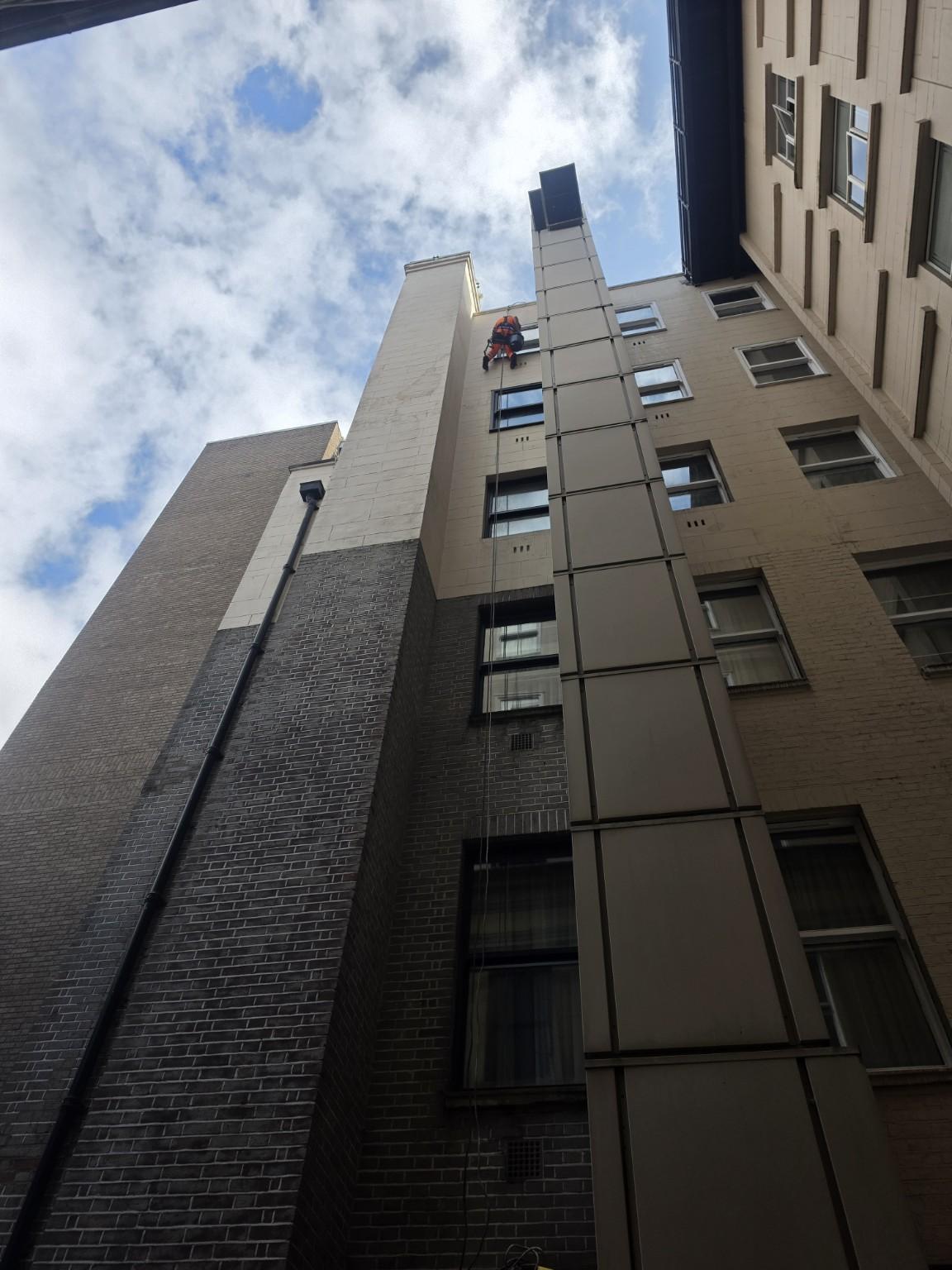 Rope access technician at a high-level window, viewed from the courtyard below