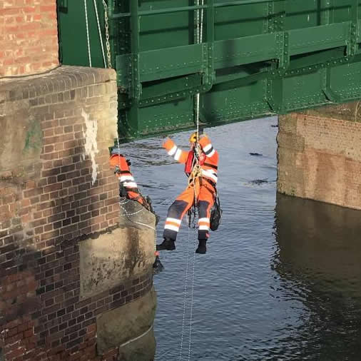 Two rope access technicians repointing the underside of a bridge