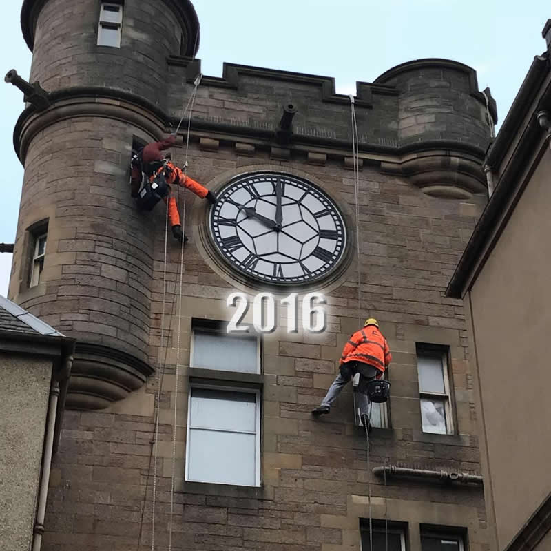 Technician abseiling to repoint a clock face on a castle-style building