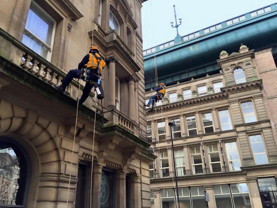 Two technicians on ropes working on an ornate city-centre building facade